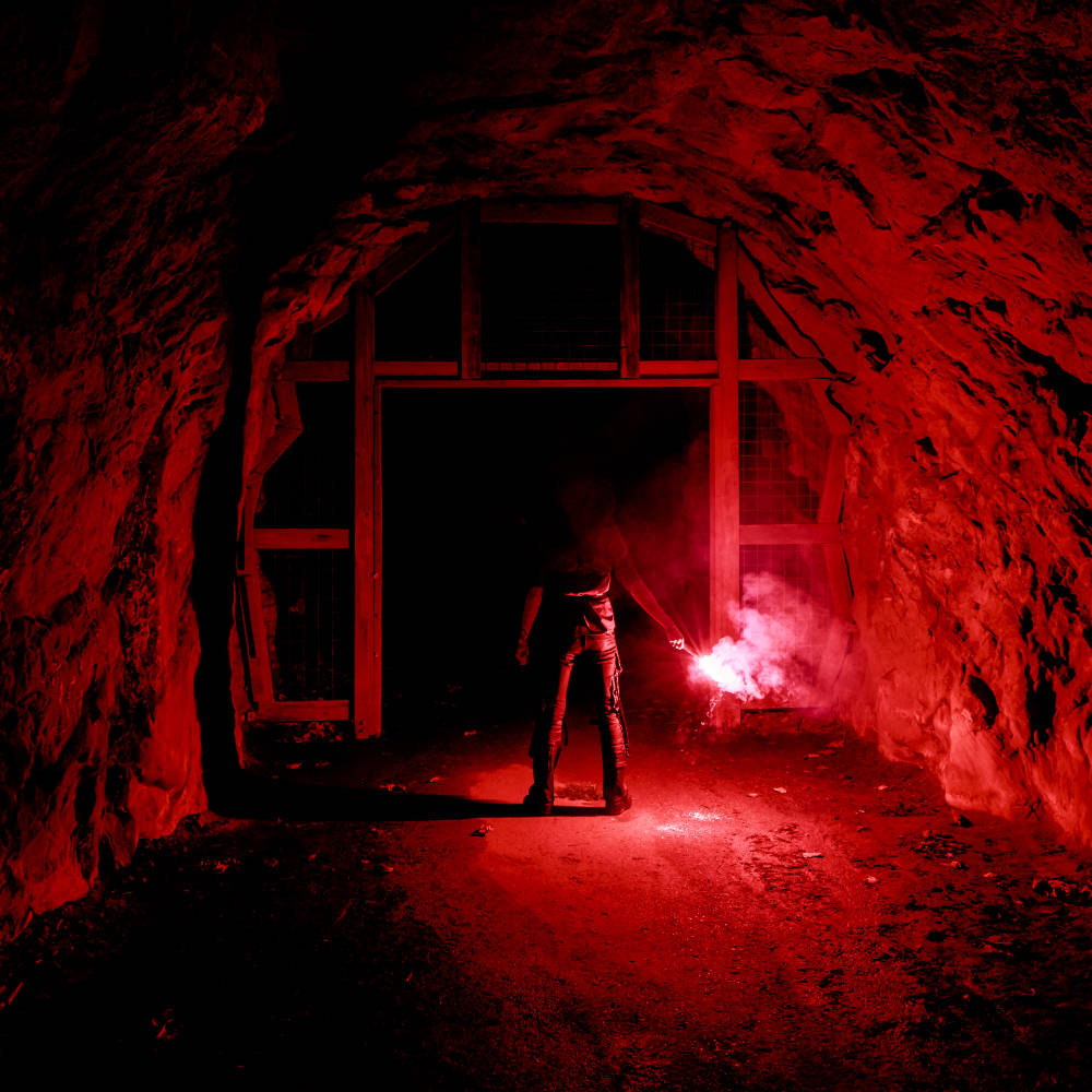Image of a man standing, facing away in a tunnel and holding a flare.