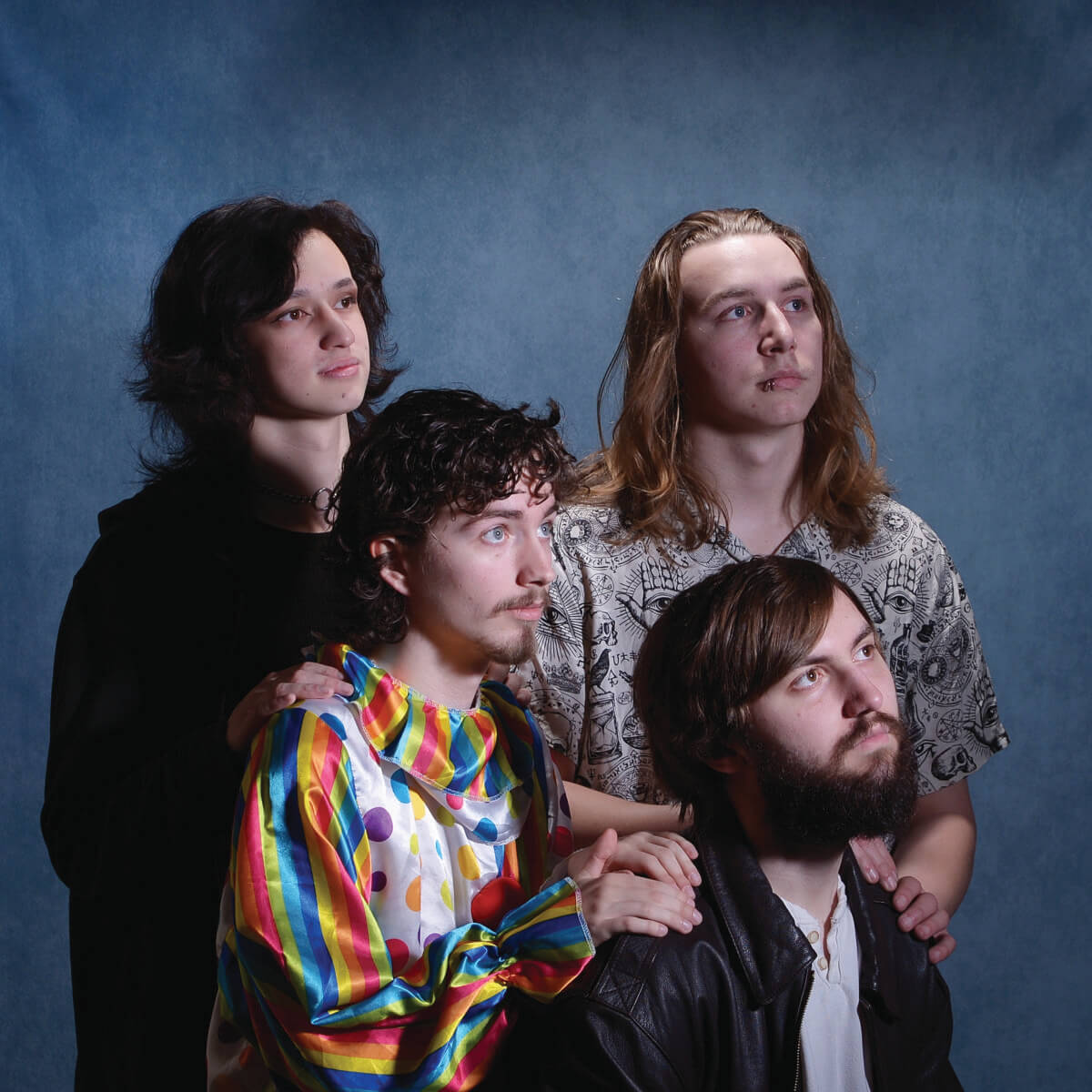 Image of four guys staring off in the distance and one is wearing a clown suite.