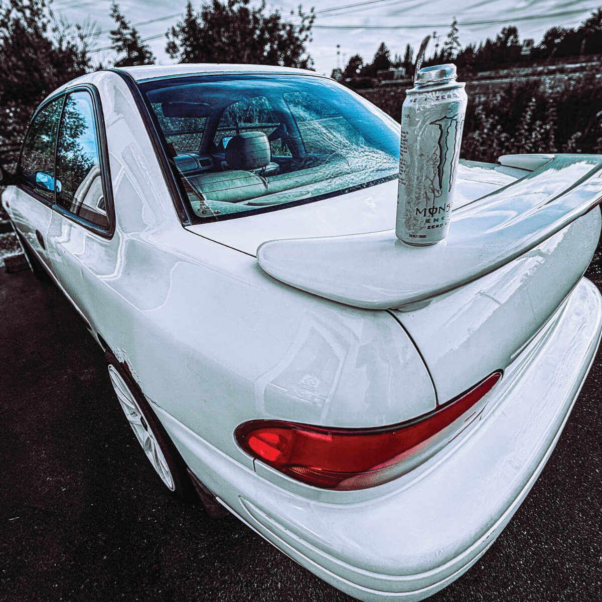 Picture of a white car with  a bottle on the back fin.
